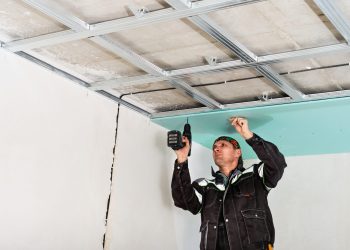 Construction worker assembly suspended ceiling with drywall and fixing the drywall to the ceiling metal frame with screwdriver.